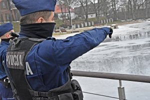 Policjant pokazuje palcem punkt na zamarznietym jeziorze