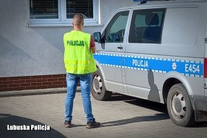 Policjant w żółtej kamizelce z napisem Policja stoi przy oznakowanym radiowozie