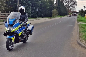 Policjant na motocyklu jedzie przed kolarskim peletonem